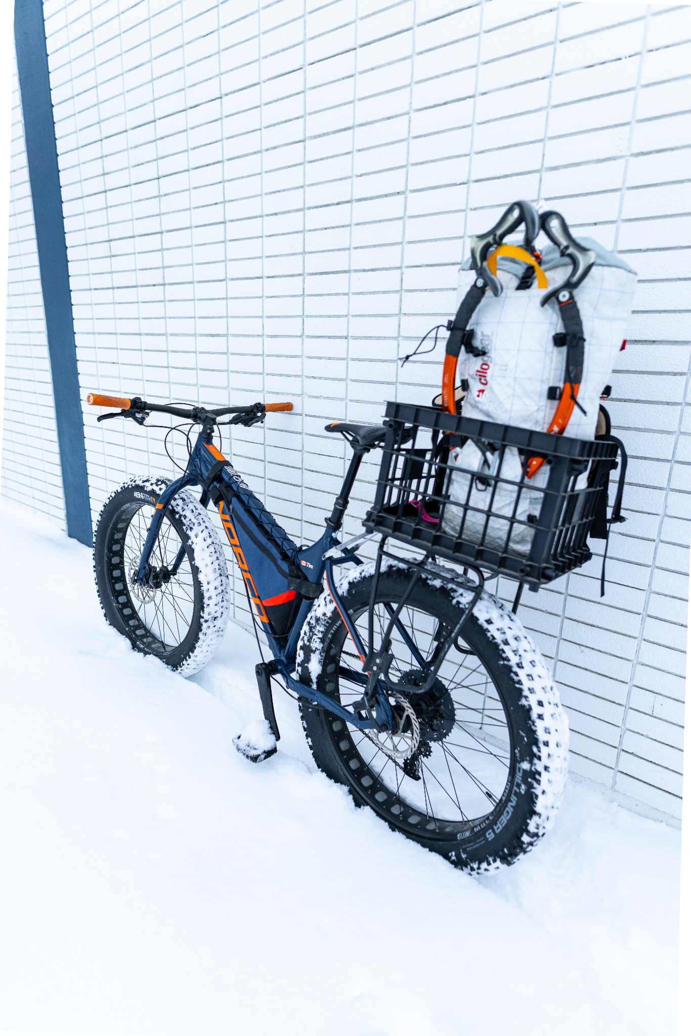 Rear view of the fat bike with a climbing pack and orange-handled ice tools upright in the crate.