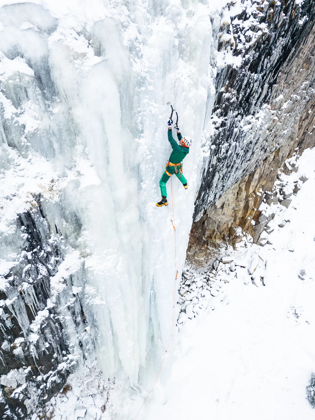 Conrad Anker climbing high on Bingo Pillar beside the dark rock wall.