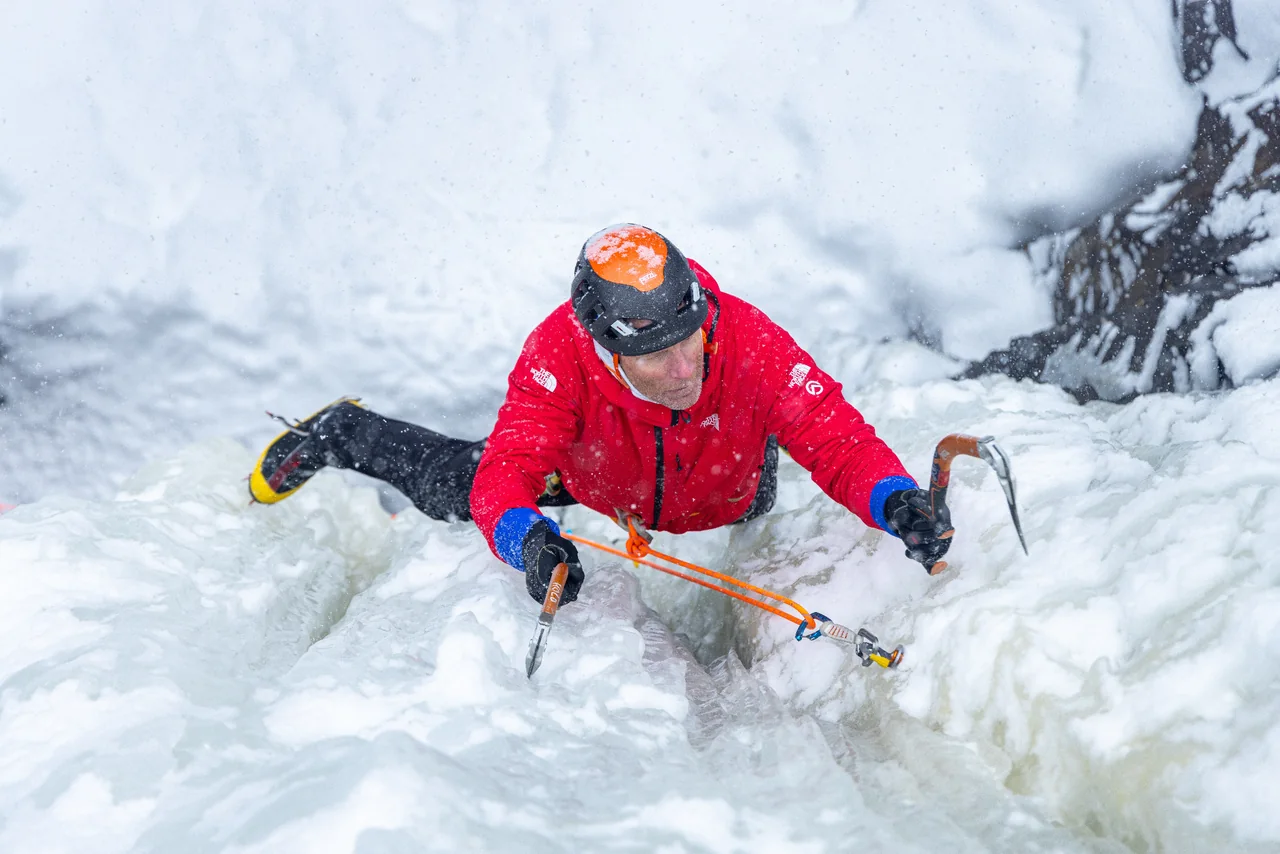 Conrad Anker stemming across ice on The Good Looking One in falling snow.