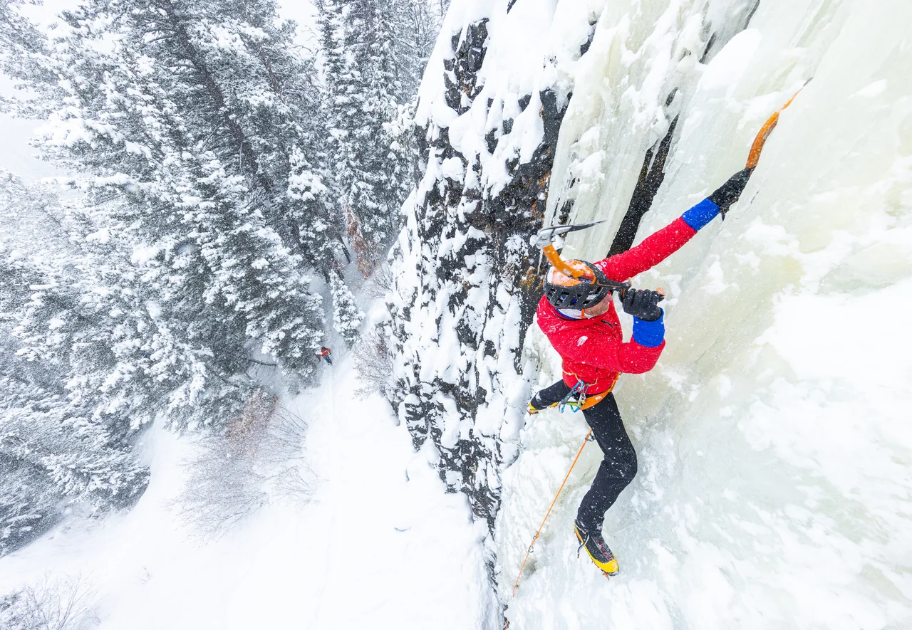 Wide view of Conrad Anker climbing The Good Looking One above the snowy forest.
